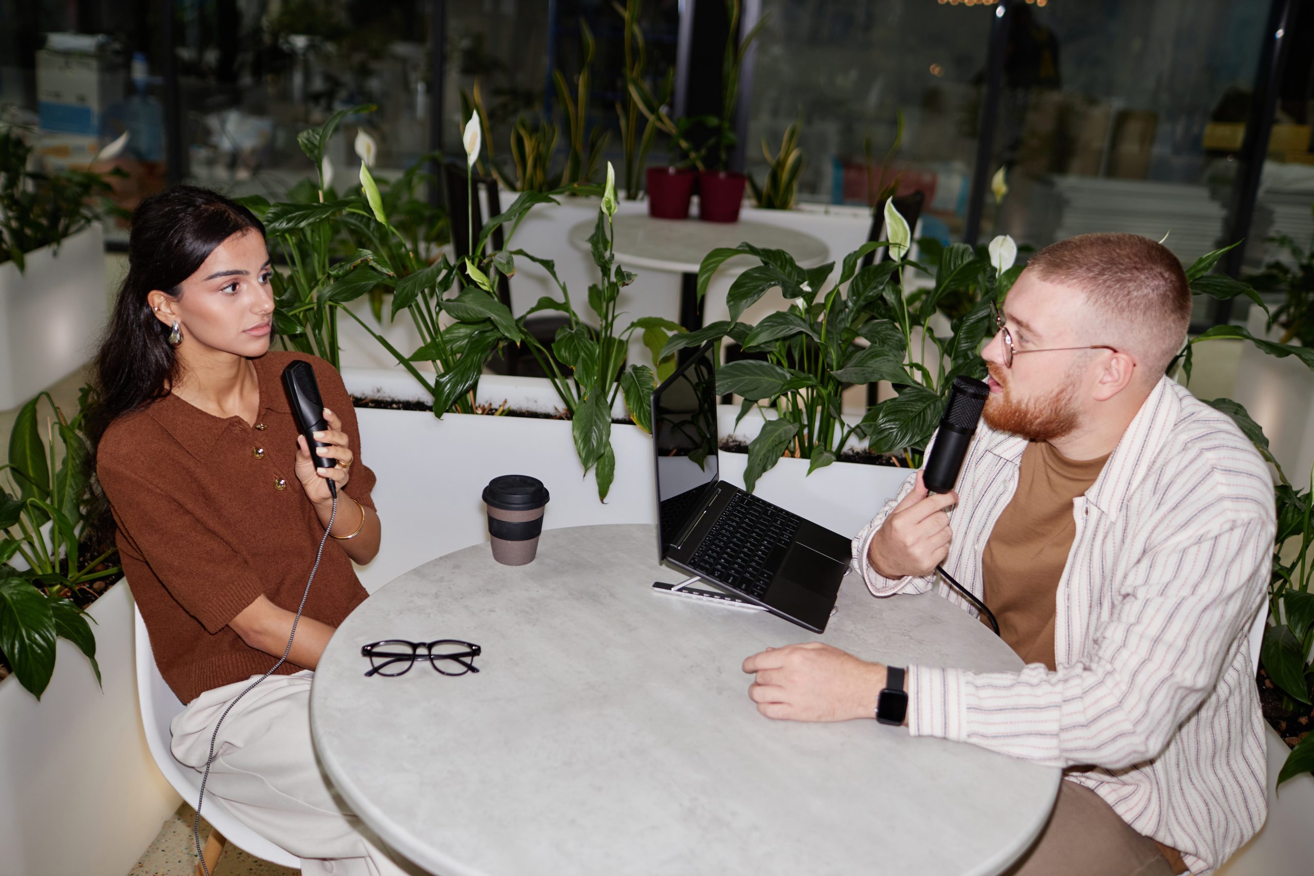 Zwei Personen sitzen an einem Tisch und nehmen einen Podcast auf.